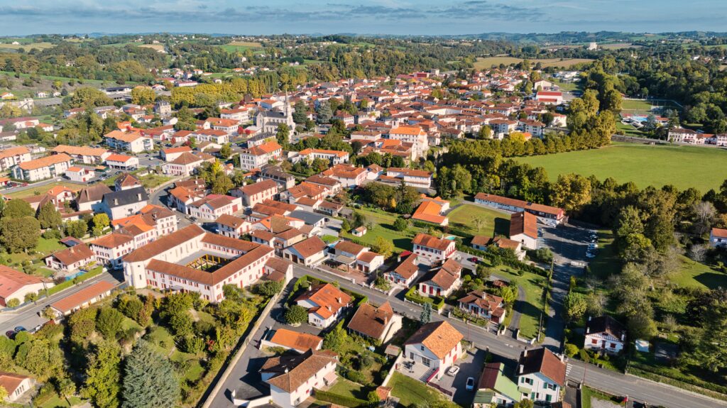 Bourg de Saint-Palais - L'image a été prise grâce à l'utilisation d'un drone. L'image est un plan large sur el bourg de Saint-Palais, on y voit l'espace culturel Bideak, l'ancienne église Saint-Paul en face de l'église de la Madeleine au milieu des maisons. On aperçoit aussi un bout du panorama en troisième plan. Crédit photo : EtxekoProd